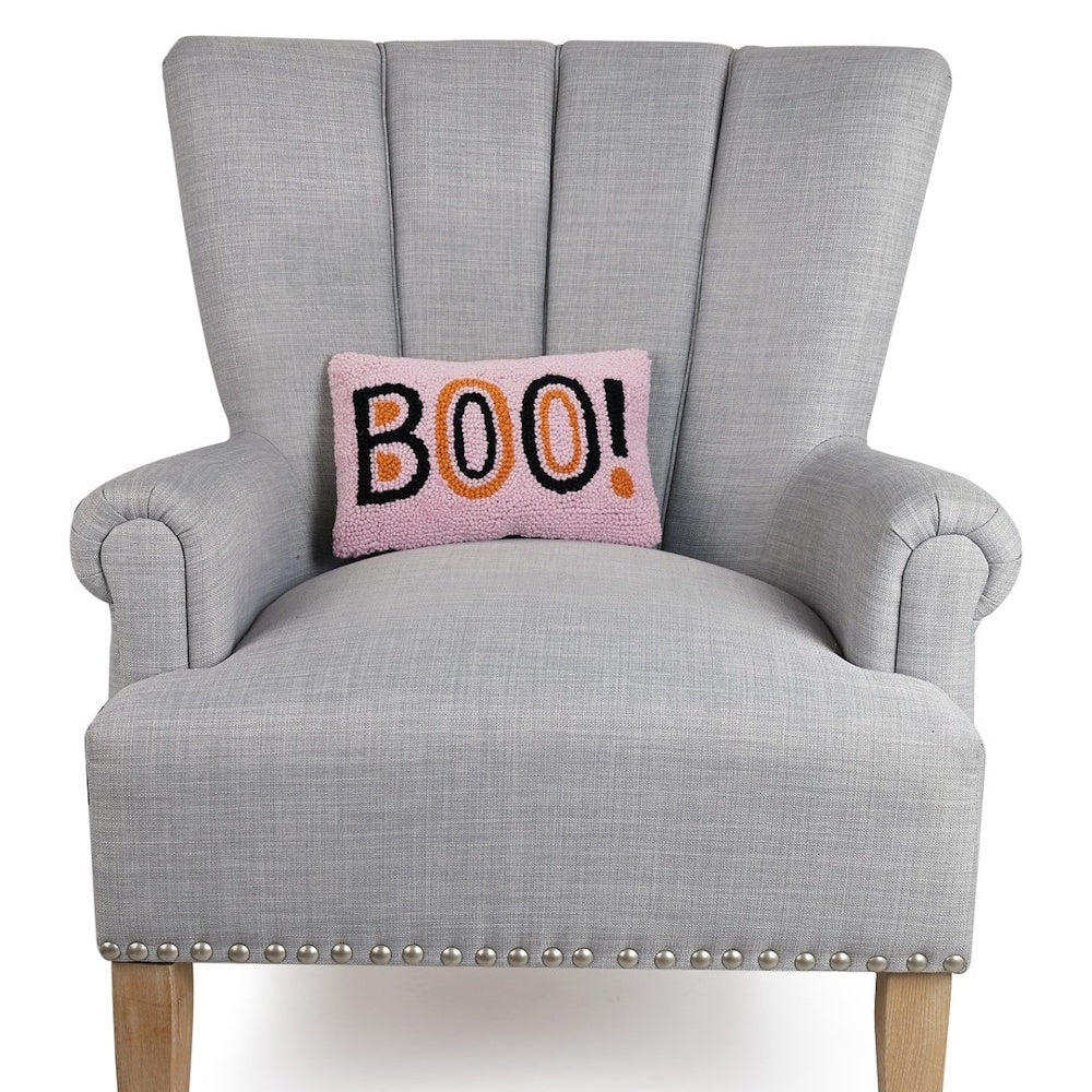 Pink hooked pillow reading "BOO!" resting on a gray, channel-tufted armchair.