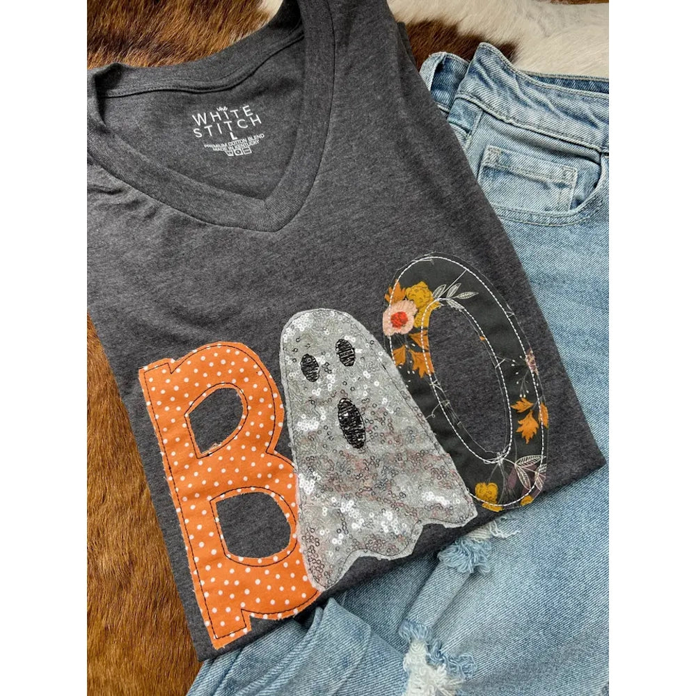 Grey V-neck t-shirt with "BOO" appliqué patchwork lying next to blue jeans.