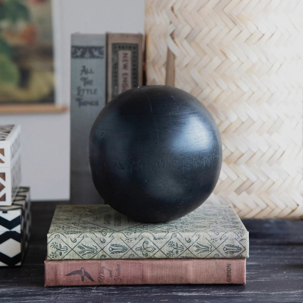 Black decorative sphere resting on vintage books like All The Little Things and Wing and Feather by Emma Gibson.