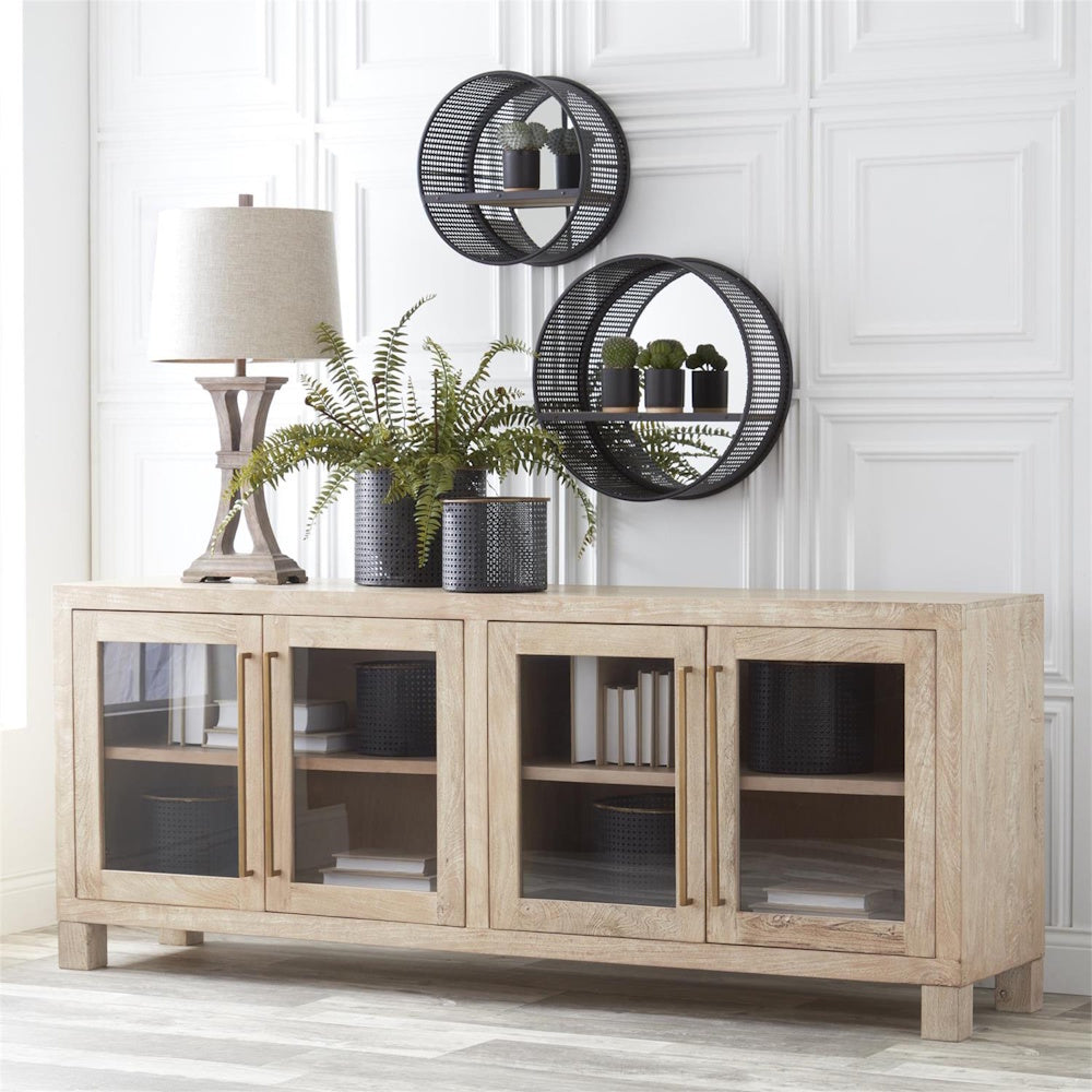 Light wood sideboard with glass doors styled with a lamp, Boston fern, and circular black metal wall shelves.