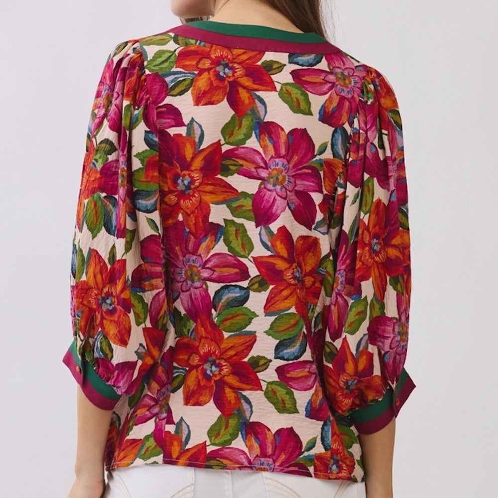 Back view of a vibrant floral blouse featuring red and pink flowers, puffed sleeves, and green trim.