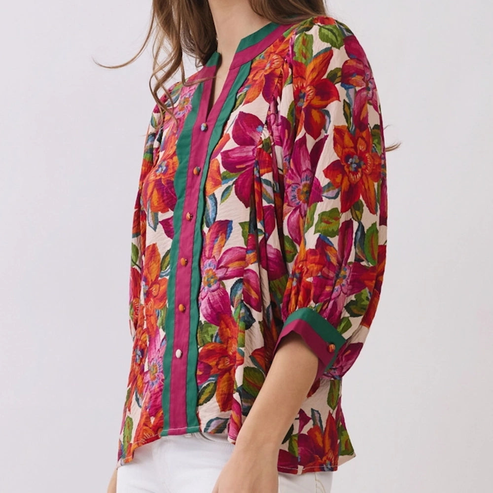 Side-profile view of a vibrant floral print blouse with green and pink trimmed placket and cuffs.
