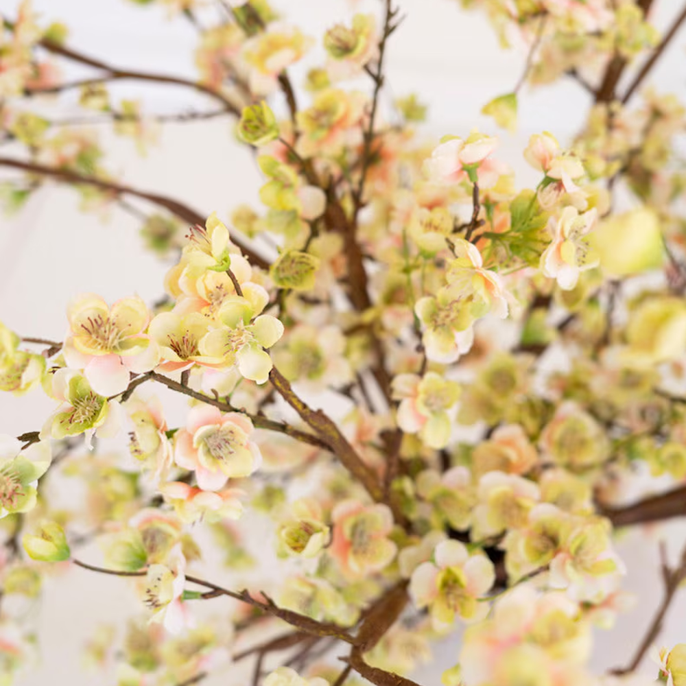 Close-up of artificial cherry blossom branches with pale yellow and pink flowers on dark brown stems.