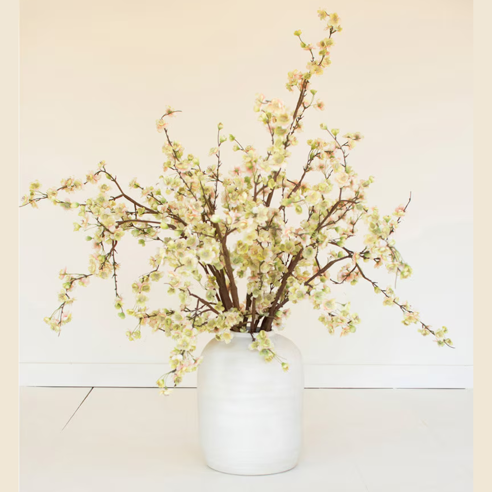 White ceramic vase with artificial flowering branches featuring pale green and pink blossoms.