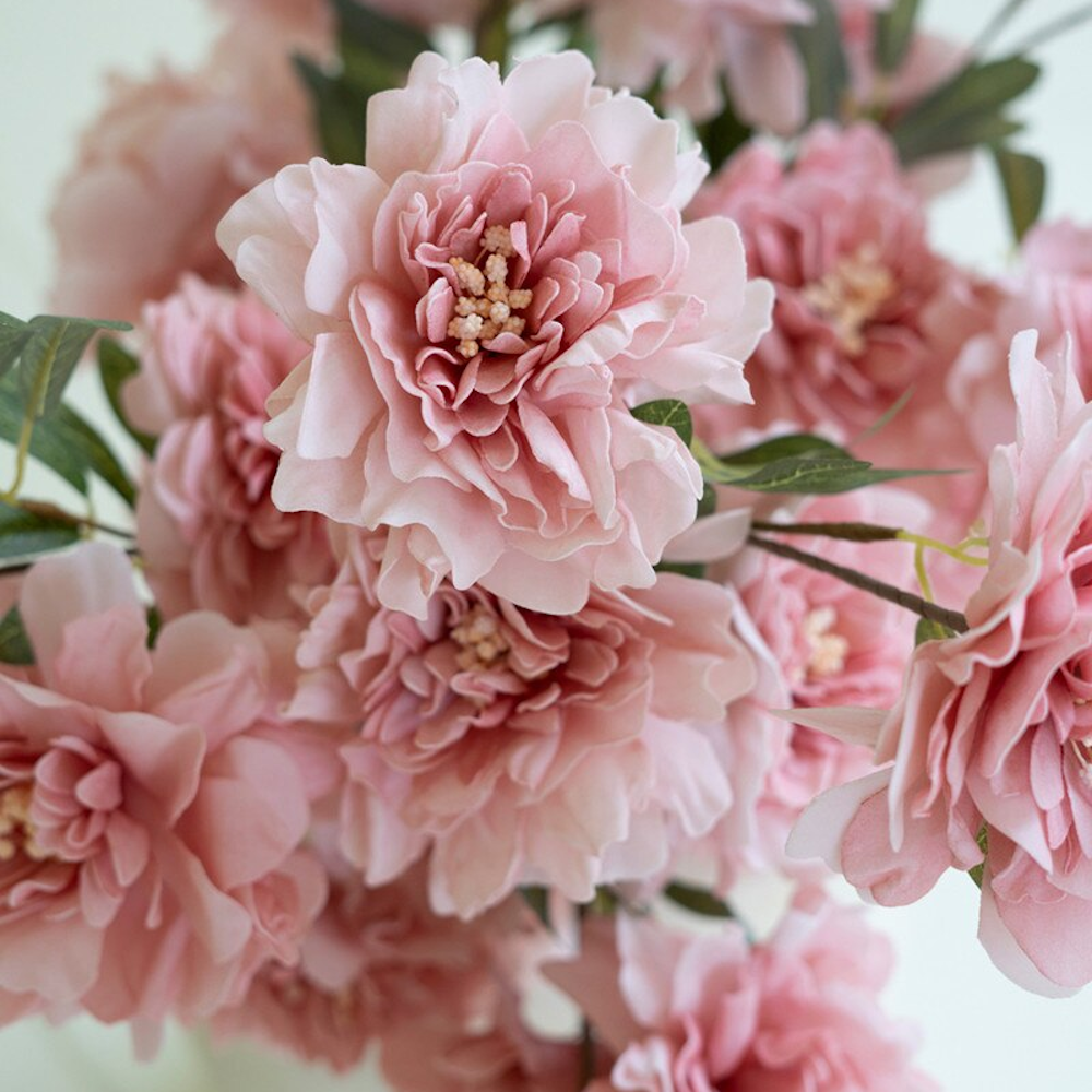 Close-up of pink silk peony blossoms with green leaves, featuring soft ruffled petals and realistic cream centers.