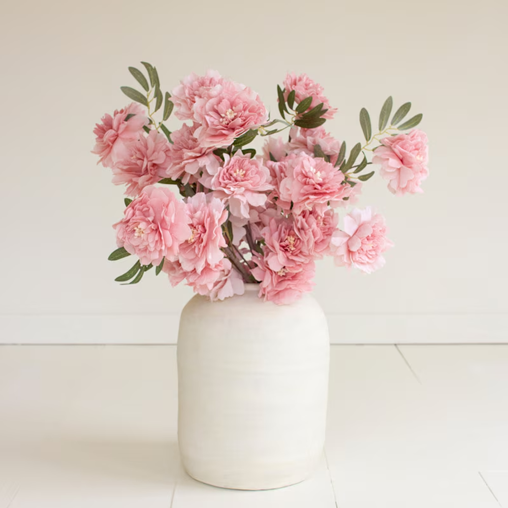 Pink faux peony arrangement in a white ceramic vase on a white floor.