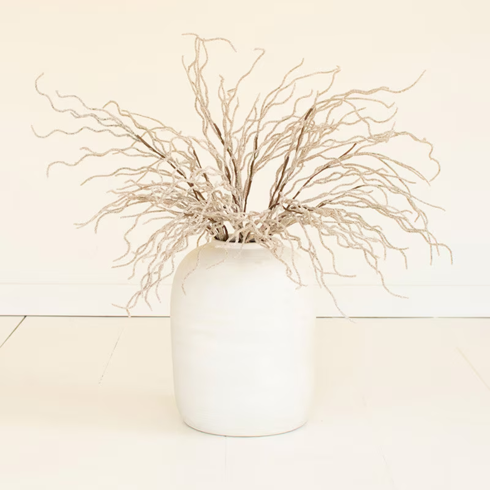 White ceramic vase with decorative curly willow branches on a white floor.