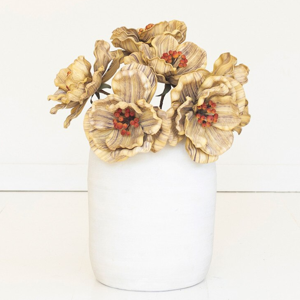 Textured yellow artificial flowers with red centers arranged in a white ceramic pot.