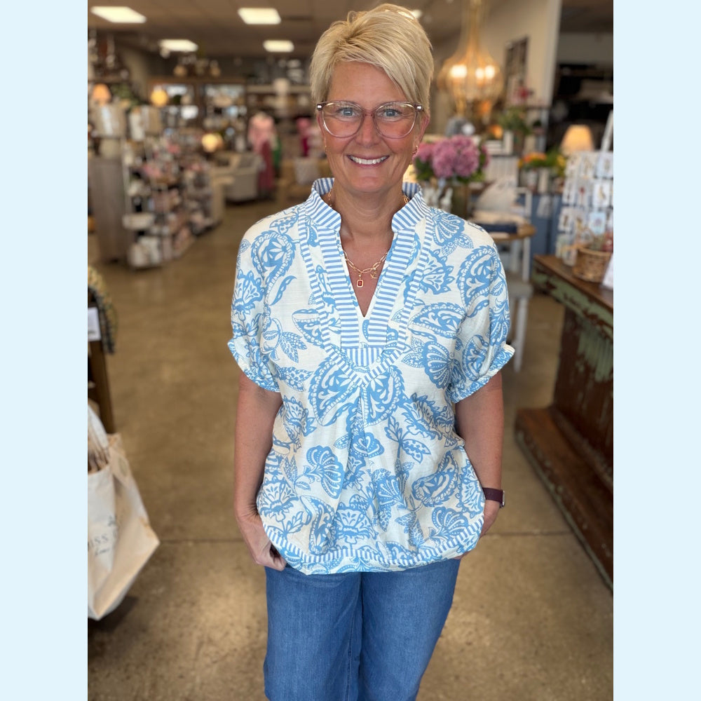 Woman wearing a blue and white botanical print tunic top with a striped neckline and blue jeans in a boutique.