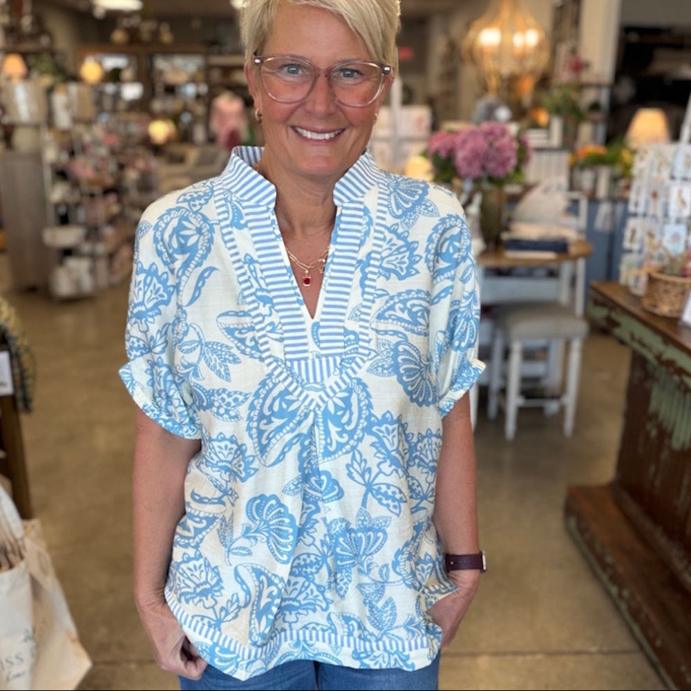 Woman wearing a blue and white botanical print tunic top with striped neckline detailing.