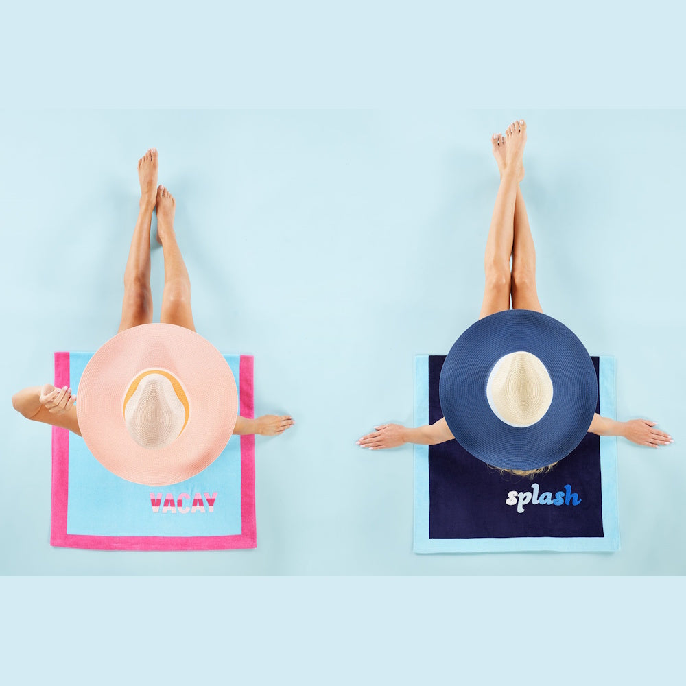 Two women in sun hats lounging on "Vacay" and "Splash" bouclé beach towels, top-down view on a light blue background.