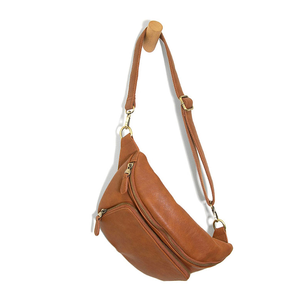 Tan leather crossbody fanny pack with adjustable strap and brass zippers, hanging on a wooden wall peg.
