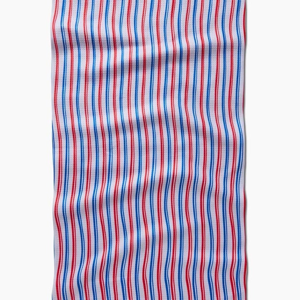 A white rectangular tea towel featuring a pattern of vertical red and blue stripes with a subtle wavy texture.