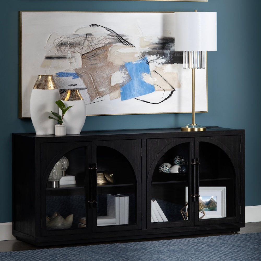 Modern black wood sideboard with arched glass doors, abstract wall art, and a gold table lamp in a blue living room.
