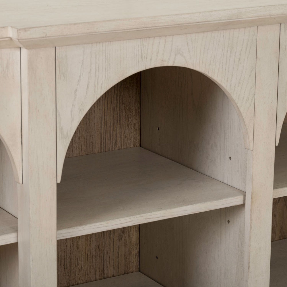 Close-up of a white washed wood breakfront accent cabinet with arched open shelving.
