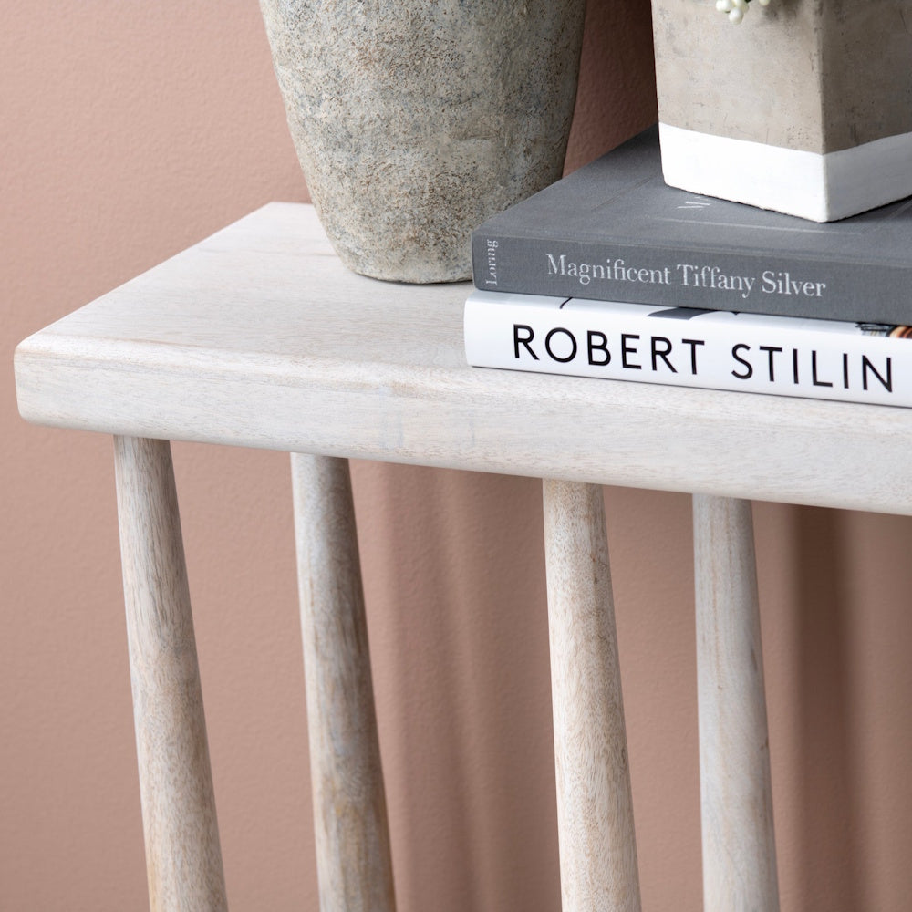 Modern white wash wood console table with decorative books and stone vases against a mauve pink wall.