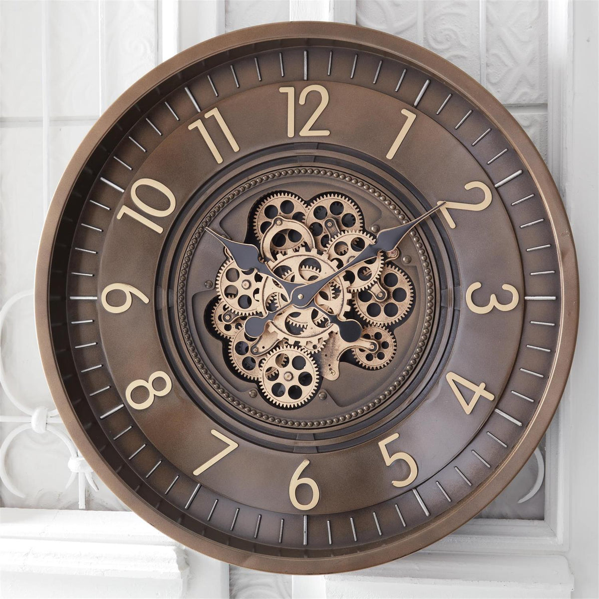 Round bronze wall clock with exposed center gears mounted on a white wall.