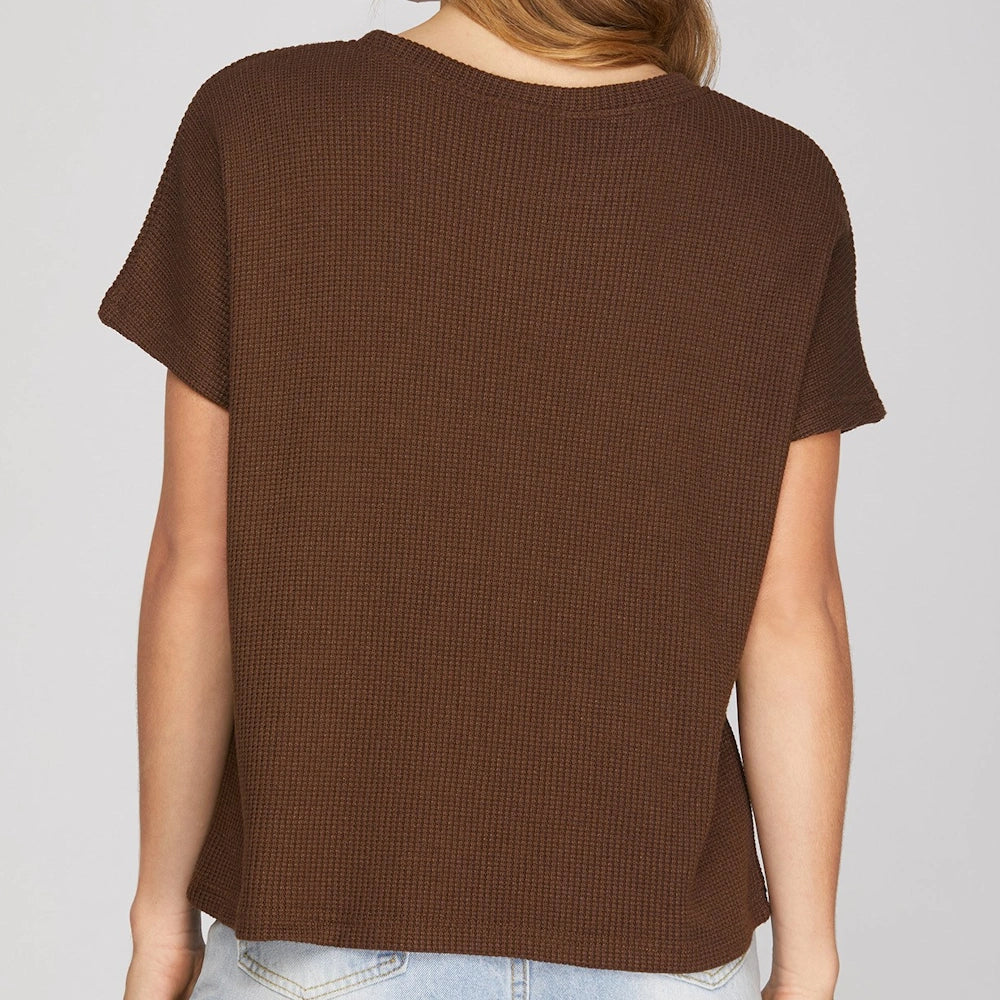 Back view of a woman wearing a brown waffle-knit short sleeve top with drop shoulders.