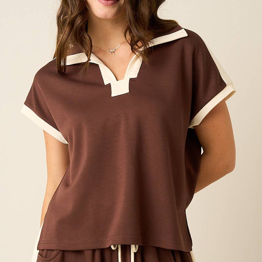 Woman wearing a brown short-sleeve polo shirt with ivory contrast trim on the collar, v-neck, and cuffs.