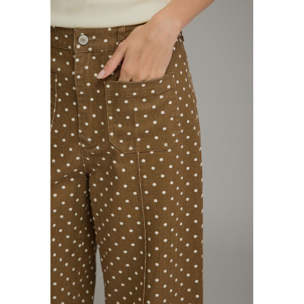 Close-up of brown polka-dot pants showing a front patch pocket with a hand inside and seam details.