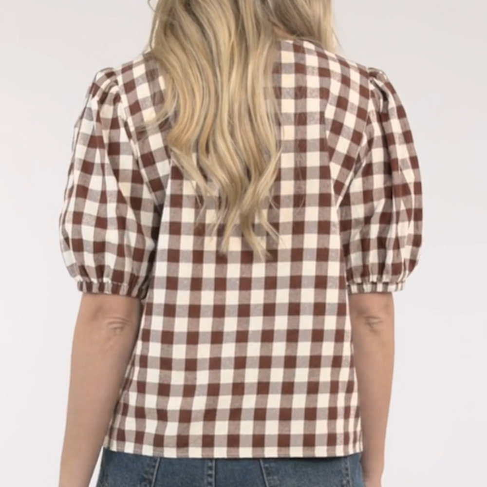 Back view of a woman wearing a brown and white gingham checked top with short puff sleeves.