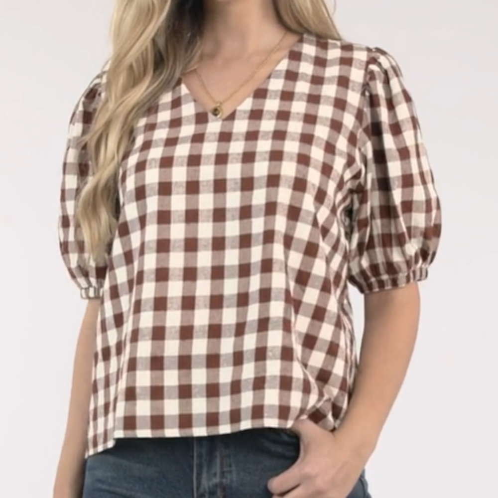 Woman wearing a brown and white gingham checked blouse with a V-neckline and short puff sleeves.