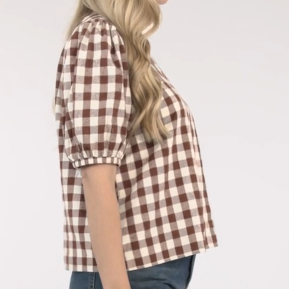 Side view of a woman wearing a brown and white gingham checked blouse with short puff sleeves and jeans.