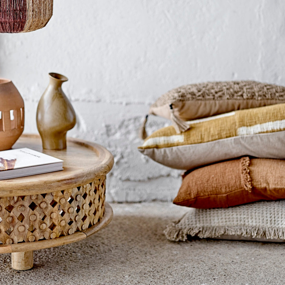 Organic-shaped ceramic vases on a carved wooden table next to a stack of textured earth-toned pillows.