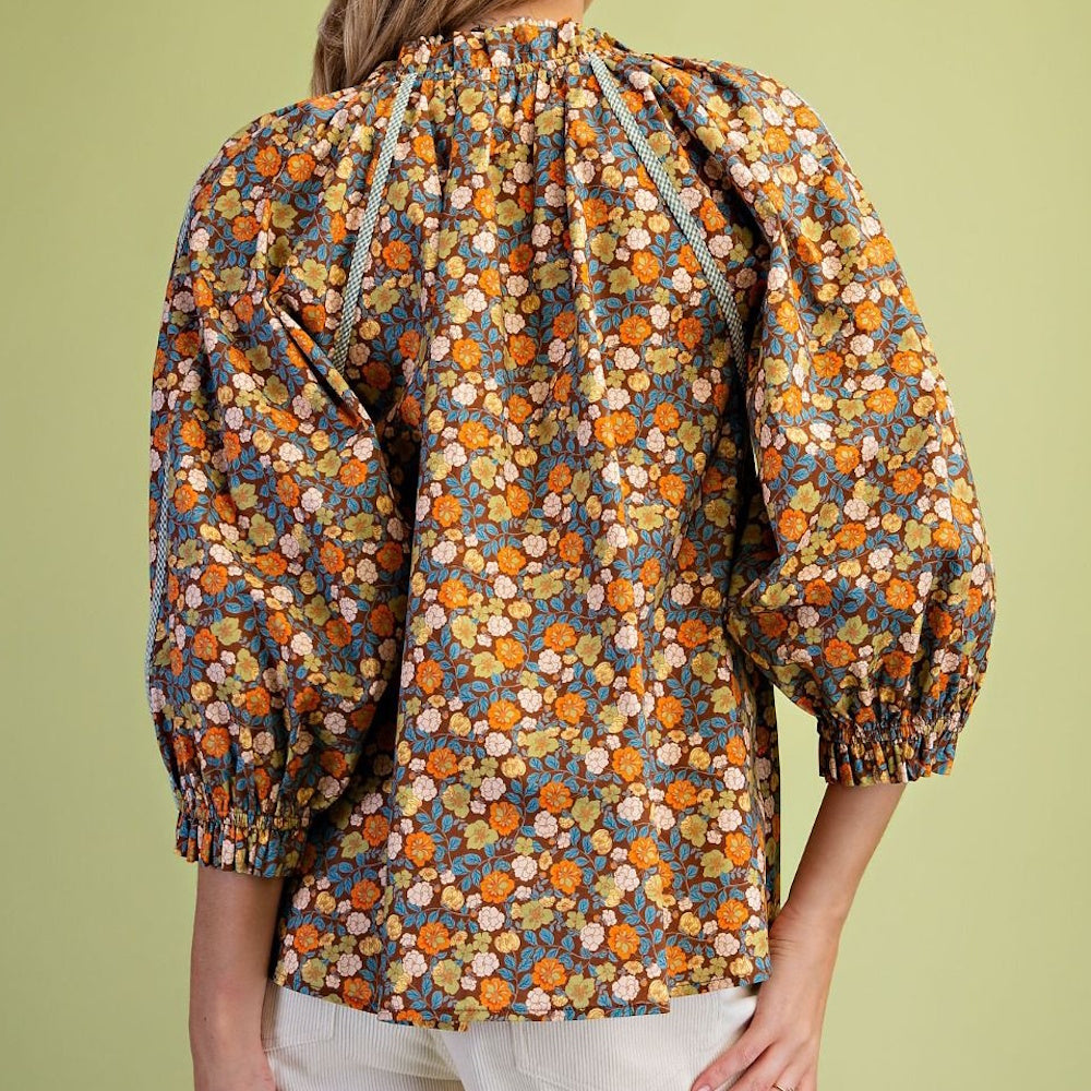 Back view of a brown floral blouse with puffy sleeves and a high gathered neckline.