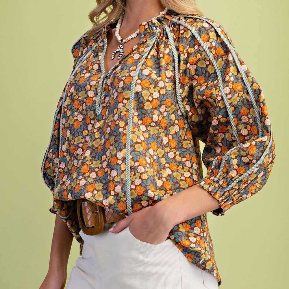 Woman wearing a brown floral puff-sleeve blouse with blue trim and white pants.