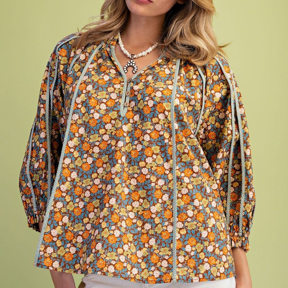 Brown, orange, and turquoise floral print boho blouse with long sleeves and light blue piping trim.