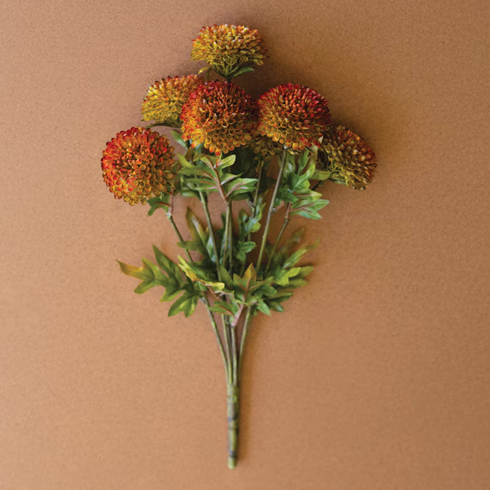 Bundle of artificial auburn ball dahlias with green leaves lying flat on a warm terracotta background.