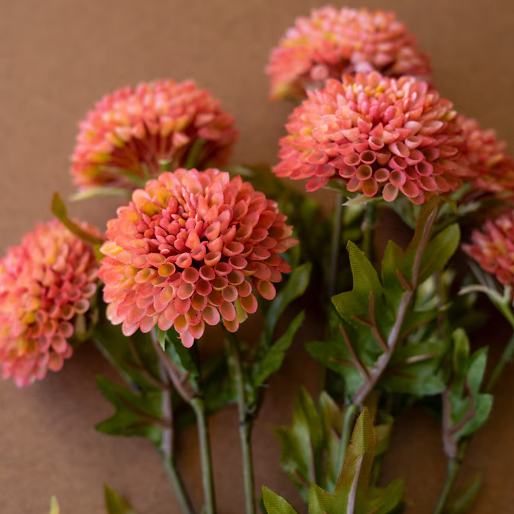 Artificial blush pink ball dahlias with green leaves and stems arranged on a brown surface.