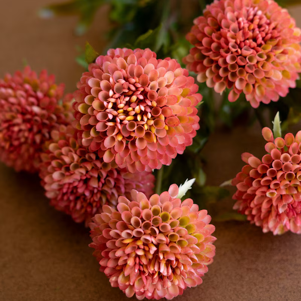 Close-up of a bundle of artificial blush pink ball dahlias with detailed petals on a brown surface.