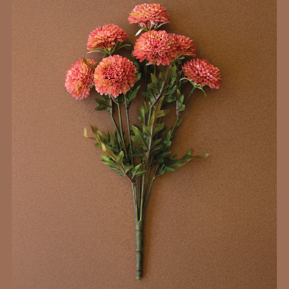 Bundle of seven artificial blush pink ball dahlia flowers on green stems against a brown background.
