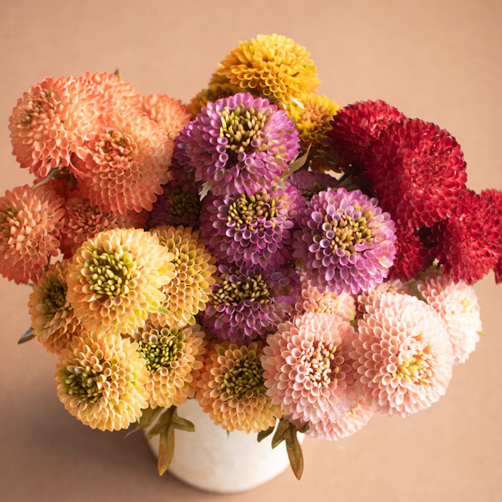 Vibrant bouquet of colorful artificial ball dahlias in pink, orange, and red arranged in a white vase.