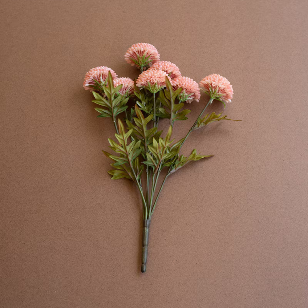 Bundle of seven artificial light pink ball dahlias with green leaves on a brown background.