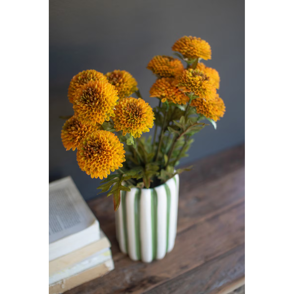 Bundles of artificial mustard yellow ball dahlias arranged in a green and white striped vase.