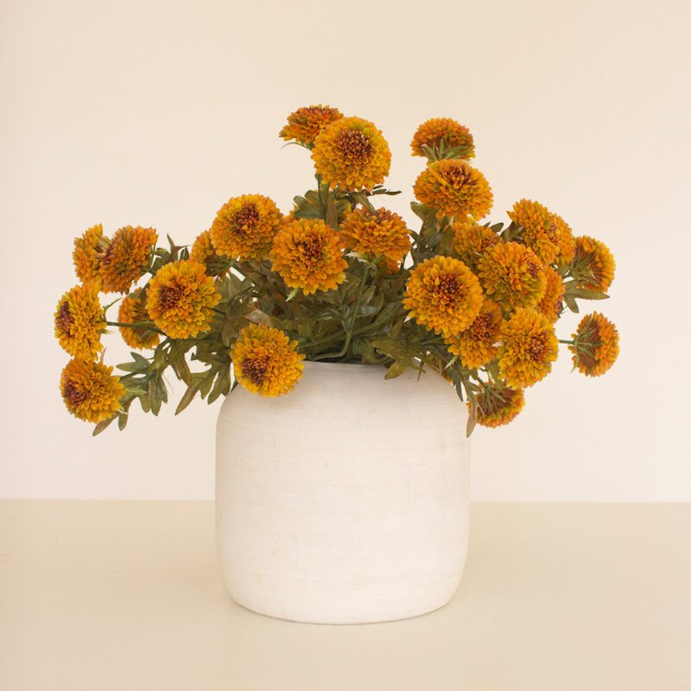Wide floral arrangement of artificial mustard yellow ball dahlias in a matte white ceramic vase.