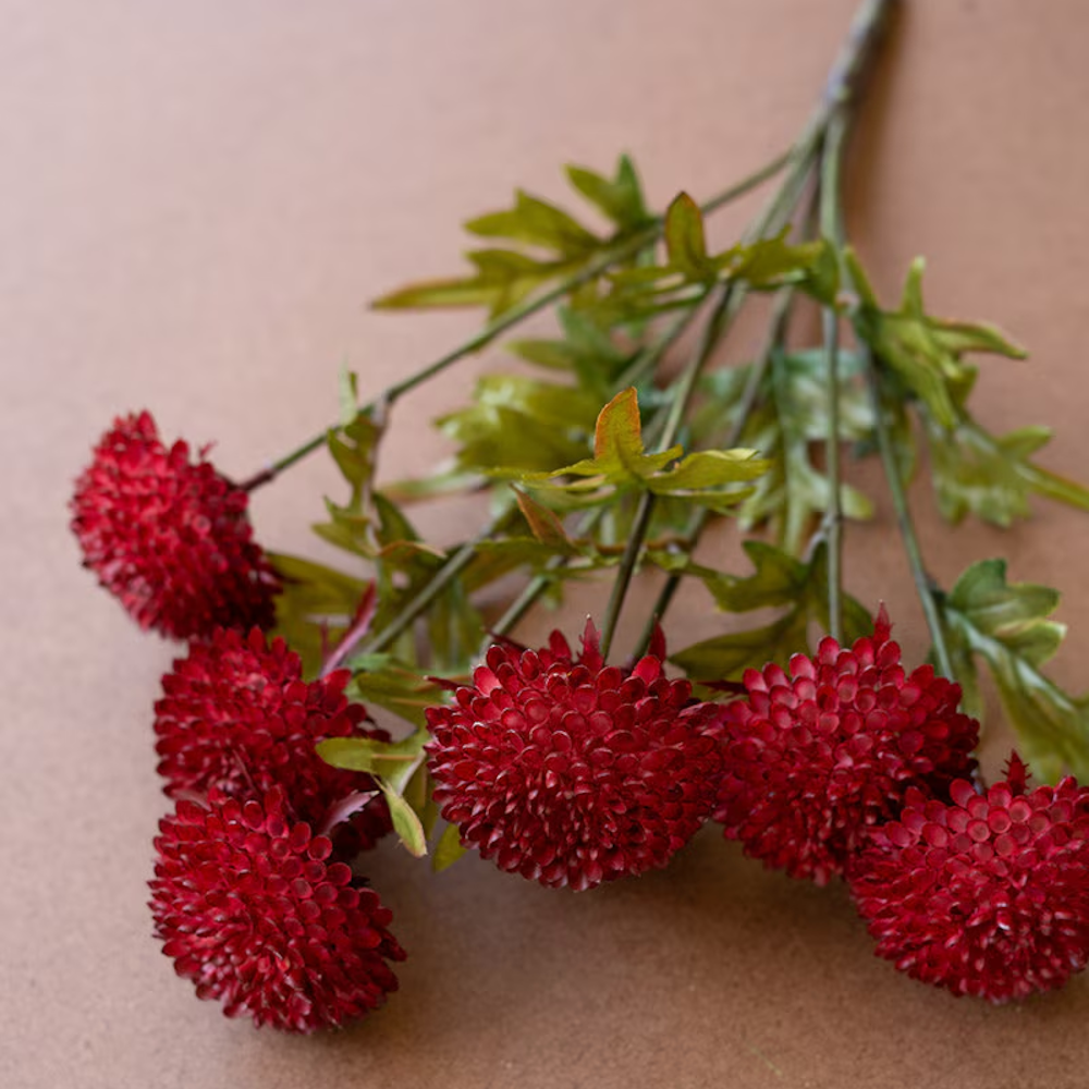 Close-up view of artificial deep red ball dahlias with green stems resting on a brown surface.