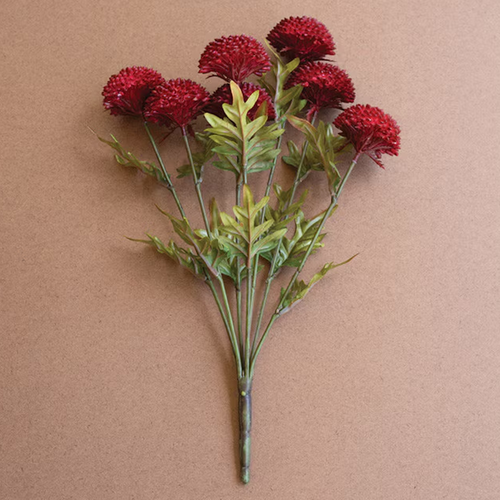 Bundle of artificial deep red ball dahlias with green leafy stems on a brown background.
