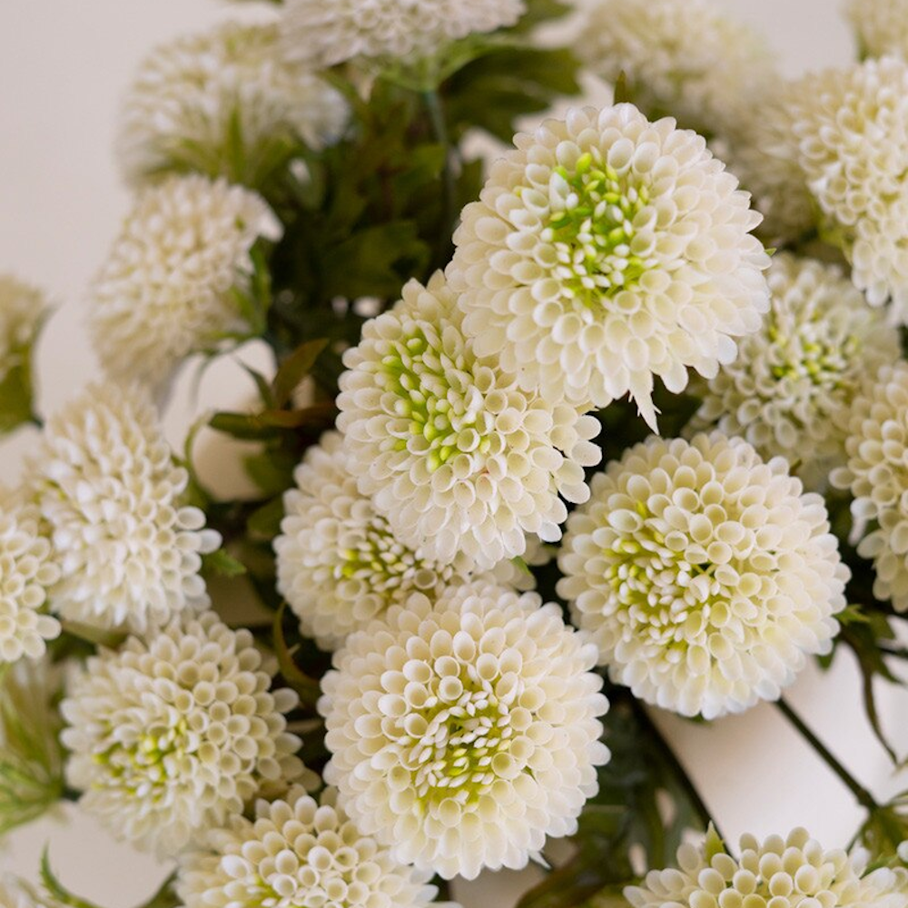 Detailed view of artificial white ball dahlias featuring rounded petal heads and soft green accents.
