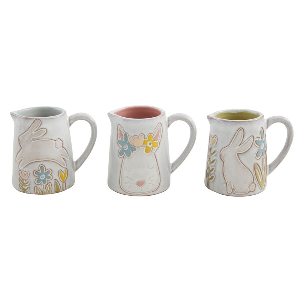 Three white ceramic mini pitchers featuring embossed bunny and flower designs with pastel accents.
