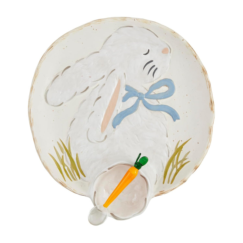 A white ceramic plate shaped with a fluffy bunny wearing a blue bow, featuring a small carrot-shaped spoon.