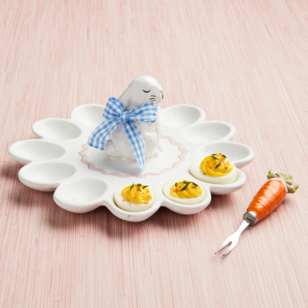 A white bunny egg platter holding three deviled eggs next to a carrot-handled serving fork.