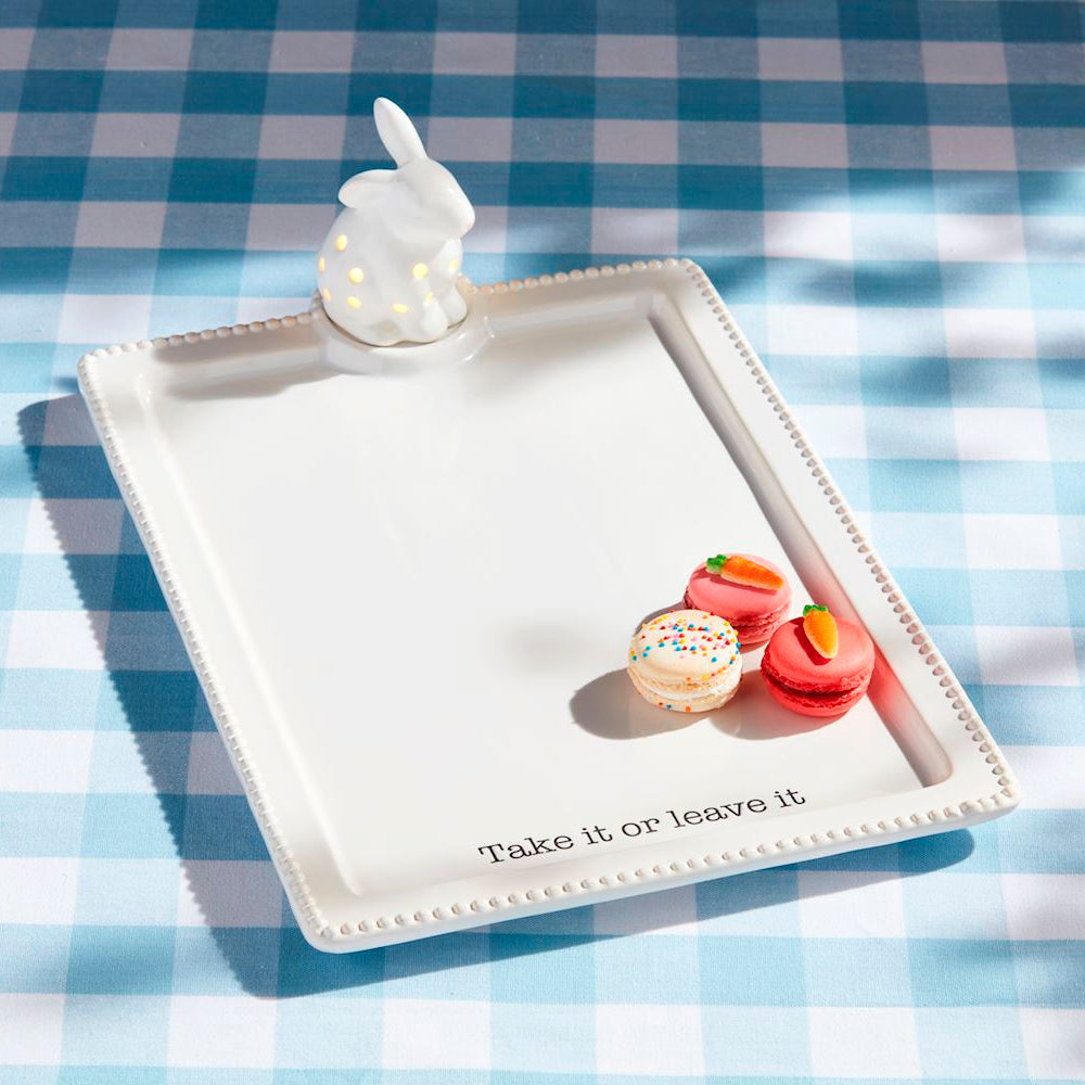 White ceramic Easter bunny serving tray with macarons and "Take it or leave it" text on a blue checkered tablecloth.
