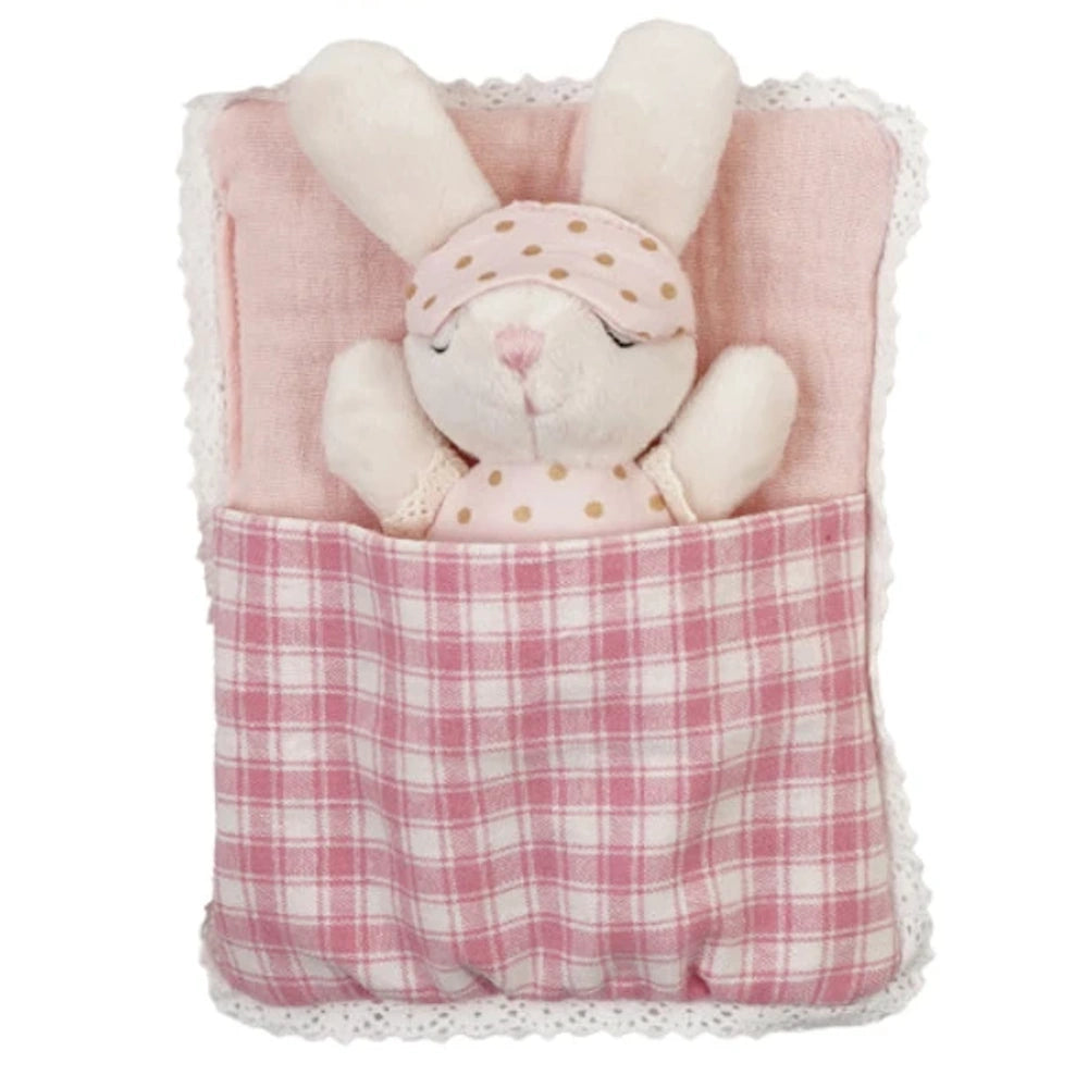 Small plush bunny wearing a polka dot eye mask sleeping in a pink plaid sleeping bag with lace trim.