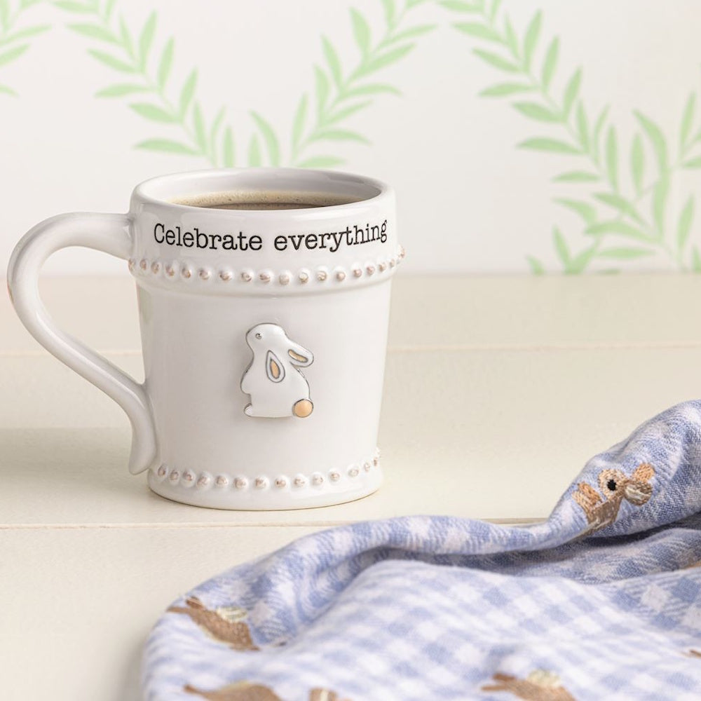 White coffee mug with "Celebrate everything" text, bunny charm, and beaded trim.
