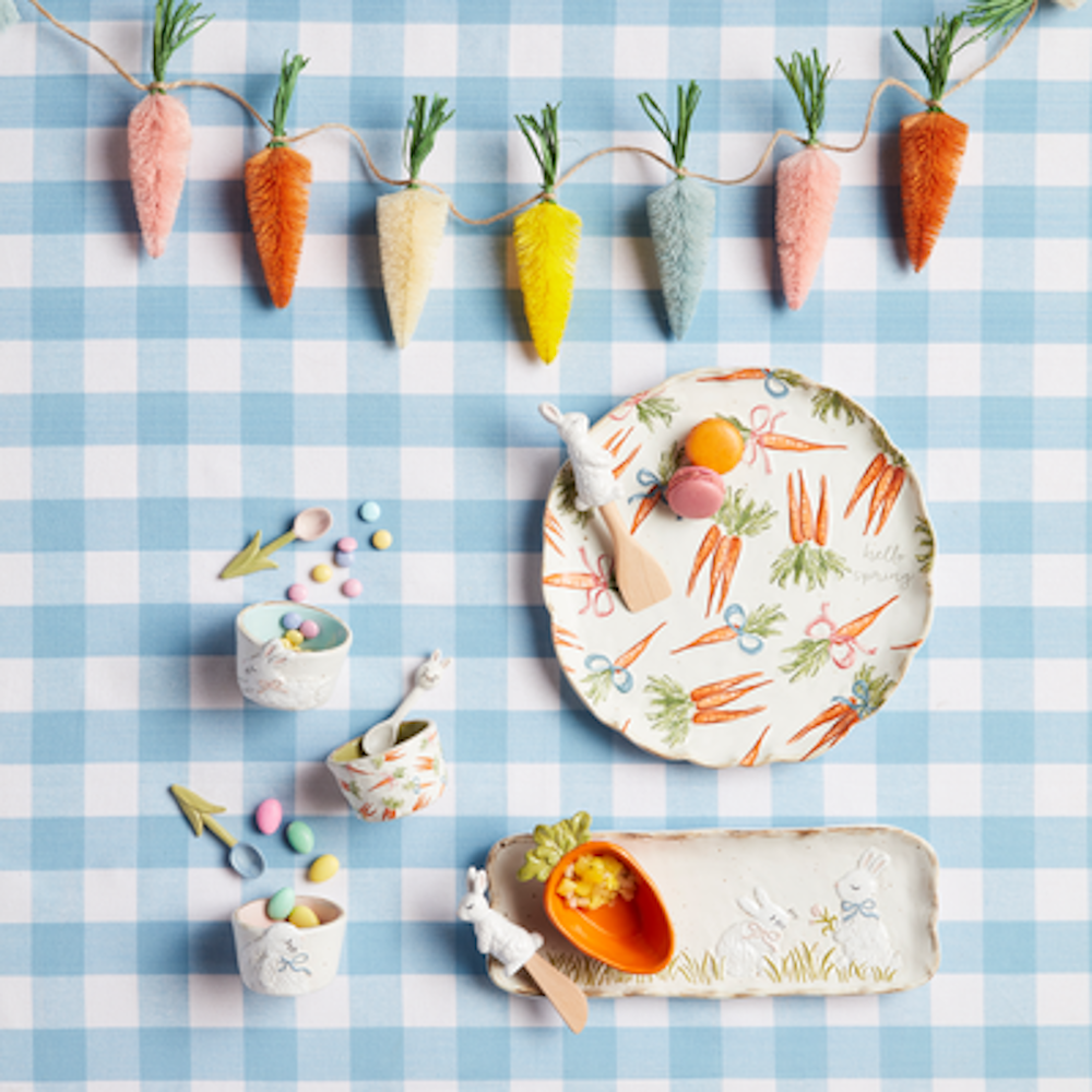 Easter and spring-themed tableware with bunny and carrot designs on a blue gingham tablecloth.