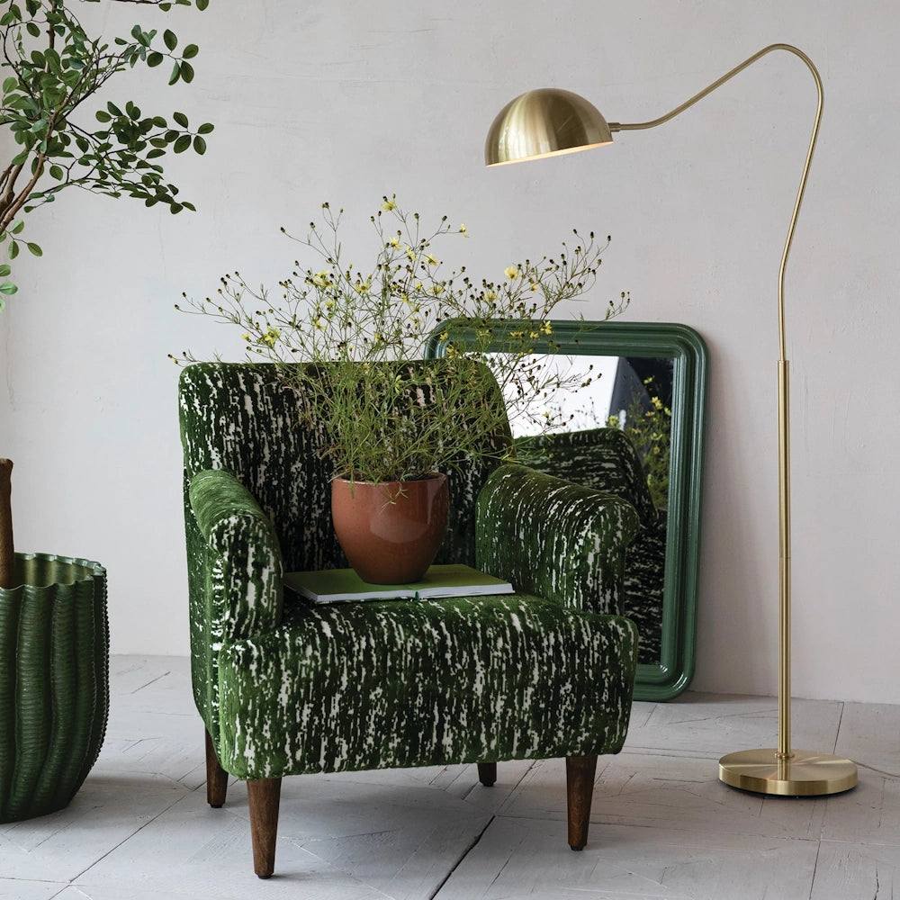 Green burnout velvet upholstered armchair with mango wood legs, styled with a gold floor lamp and potted plant.